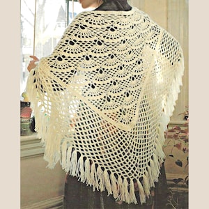 May include: A triangular off-white crochet shawl featuring a repeating fan-shaped stitch pattern across the upper section and a diamond-shaped open mesh grid on the lower portion, finished with long, dangling fringe along the bottom edges.