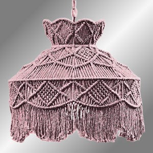 May include: A dusty rose macrame pendant light fixture. The light has a bell-shaped shade with geometric patterns and a fringed bottom edge. The light is suspended from a chain.