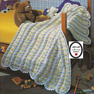 May include: A crocheted blanket featuring vertical stripes of white, light blue, and pastel rainbow yarn with small yellow bobbles. The blanket has a scalloped edge and is draped over a bed. A sign displays the text 40% off on 2 or more patterns.