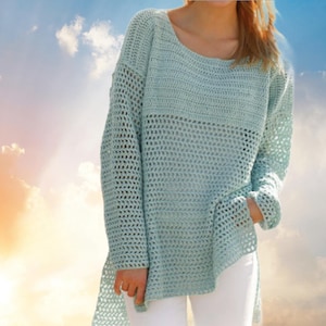 May include: A light blue crochet sweater with a loose, open weave design. The sweater has long sleeves and a slightly asymmetrical hemline. The neckline is a wide scoop, and the overall style is casual and relaxed.