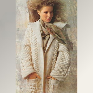 May include: Cream-coloured, hooded cardigan with a textured knit pattern. The long-sleeved sweater features a shawl collar, pockets, and a patterned scarf. The cardigan is a cosy, stylish outerwear option.