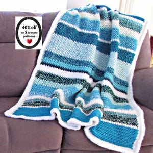 May include: A crocheted blanket featuring horizontal stripes in various shades of blue, teal, and white. The blanket has a solid white border along the edges. A small white sign with a black oval border displays the text 40% off on 2 or more patterns.