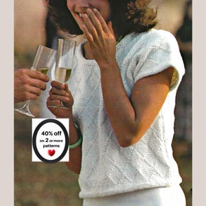 May include: A white short-sleeved knitted top featuring a textured diamond pattern throughout the fabric. A small rectangular graphic overlay is present, containing the text 40% off on 2 or more patterns and a red heart icon.