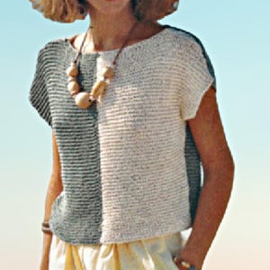 May include: A two-toned, short-sleeved top with a split design. One side is a light grey with horizontal stripes, and the other is off-white. A wooden bead necklace is worn with the top. The bottom of the top is visible, along with a portion of a yellow skirt.