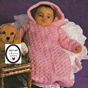 May include: A baby wearing a light pink hooded knit bunting with a textured popcorn stitch pattern and a front zipper closure. A small white sign with a black oval border displays the text 40% off on 2 or more patterns and a red heart icon.
