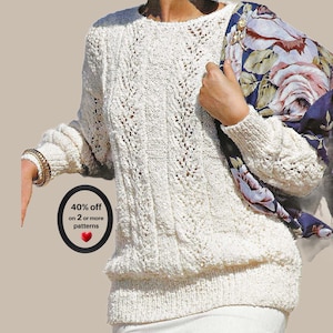 Peut inclure: Un pull à manches longues blanc cassé avec un motif complexe de torsades verticales et de dentelle. Une écharpe bleu foncé à grand motif floral rose et blanc est posée sur une épaule. Un badge circulaire noir affiche 40% off on 2 or more patterns.
