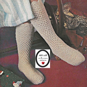 May include: A pair of beige, knee-high crochet socks featuring a textured, woven stitch pattern. A small rectangular sign is positioned between the socks, displaying the text 40% off on 2 or more patterns with a red heart icon.
