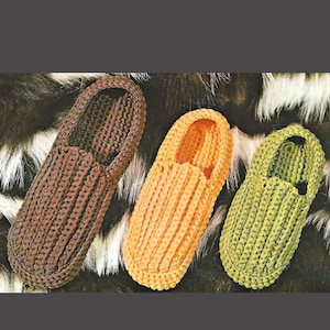 May include: Three knitted slippers in shades of brown, orange, and green. The slippers have a ribbed texture and a simple, classic design. The slippers are displayed on a textured background.