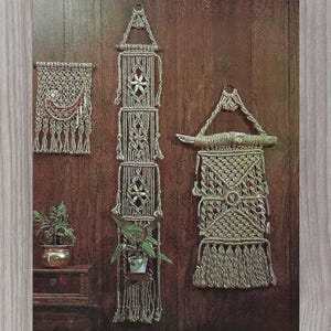 May include: A collection of macrame wall hangings in various sizes and designs. The pieces are made of natural-colored rope and feature geometric patterns, fringe, and plant holders. The hangings are displayed against a wood-paneled wall.
