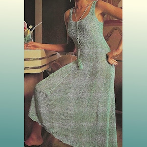May include: A light green, sleeveless maxi dress with a textured knit pattern. The dress has a scoop neckline and a flowing skirt. A long necklace with a tassel is worn with the dress. The dress is a vintage style.