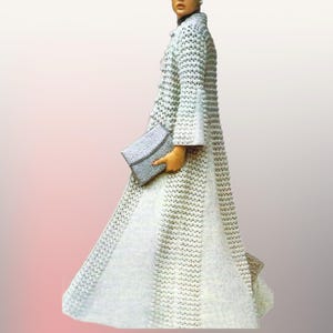 May include: A long, white crocheted coat with bell sleeves and a button-down front. The coat is paired with a small, light-coloured clutch. The garment has a textured appearance and a flowing skirt. The background is a gradient of pink and white.