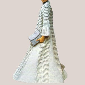 May include: A long, white crocheted coat with bell sleeves and a matching clutch. The coat features a button-down front and a flared skirt. The clutch is a light gray color. The coat is a vintage style.