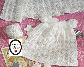 May include: A white knitted baby set featuring a dress with short sleeves, a matching bonnet, and a pair of booties. The set includes a white knitted blanket with a textured pattern. A small sign displays the text 40% off on 2 or more patterns.
