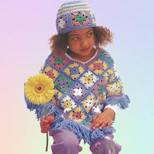 May include: A vibrant, crocheted poncho and hat set. The poncho is patterned with squares in blue, yellow, pink, and green, finished with a fringed edge. The hat mirrors the design. A yellow flower is held in the hand.