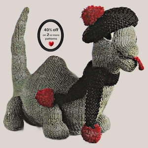 Op de afbeelding: Een gebreid dinosaurus speeltje in groentinten, met een zwarte baret met een rode pompon, een zwarte sjaal en rode pompons aan de voeten. Een rode tong steekt uit de mond. De tekst luidt: 40% off on 2 or more patterns met een rood hartje.