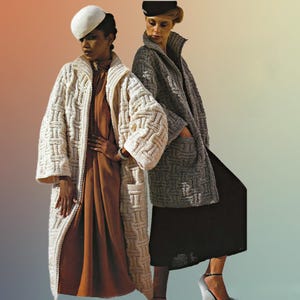 Könnte beinhalten: Zwei Frauen, die lange, strukturierte Strickmäntel tragen. Einer ist cremeweiß, der andere grau. Beide Mäntel haben große Taschen und ein geometrisches Muster. Die Frau links trägt einen weißen Hut und ein braunes Kleid. Die Frau rechts trägt einen schwarzen Hut und einen schwarzen Rock.
