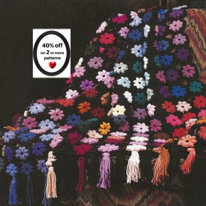 May include: A black crochet blanket featuring a repeating pattern of multi-coloured floral motifs in shades of pink, blue, purple, orange, and white. The bottom edge is finished with a row of long, dangling yarn tassels in matching colours.