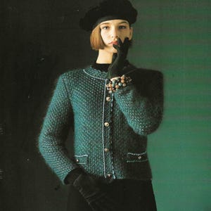 May include: A teal green knit jacket with a textured pattern, white trim, and gold buttons. The jacket has two front pockets and is paired with a black beret and gloves. A beaded bracelet adorns the wrist.