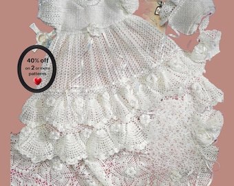 May include: A white knitted dress with short sleeves, a ruffled skirt, and matching bonnet. The garment features intricate lace-like patterns, small floral accents, and thin ribbon ties. A black circular graphic displays the text 40% off on 2 or more patterns.