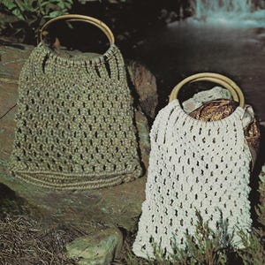Può includere: Due borse in macramè con manici in legno. Una borsa è verde oliva chiaro, l'altra è bianco sporco. Entrambe le borse hanno un design traforato intrecciato. Le borse sono appoggiate su una grande roccia, con vegetazione in primo piano.
