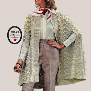 May include: An off-white cable knit cape with a textured bobble pattern, worn over a white collared button-down shirt, a red and white patterned neck scarf, and brown plaid trousers. A black oval badge displays the text 40% off on 2 or more patterns.