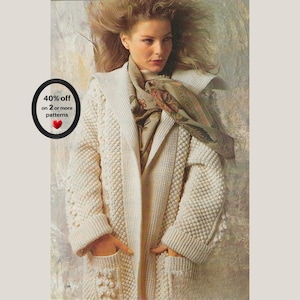 May include: An off-white, long-sleeved, open-front knit cardigan featuring a textured bobble stitch pattern, wide lapels, and two front pockets. A floral-patterned scarf in shades of brown, green, and orange is draped around the neck.