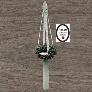 May include: A cream-coloured macrame plant hanger featuring intricate knotted cord patterns, a central circular opening for a pot, and a long decorative fringe at the bottom. A white sign displays the text 40% off on 2 or more patterns with a red heart.