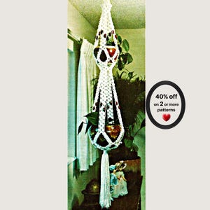 May include: A white macrame plant hanger with two tiers designed to hold pots, featuring knotted cord construction, dark brown wooden beads integrated into the pattern, and a long decorative tassel at the bottom. Text reads: 40% off on 2 or more patterns.