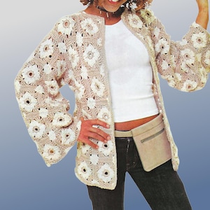 May include: A beige and white crochet jacket with a floral pattern. The jacket has long sleeves and a collarless design. The model is wearing a white top, dark jeans, and a beige fanny pack. The jacket is open in the front.