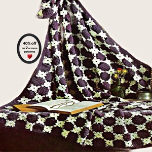 May include: A dark purple crocheted blanket featuring a repeating pattern of white floral motifs. An open book with wire-rimmed glasses rests on the blanket. Text on the image reads 40% off on 2 or more patterns with a small red heart icon.