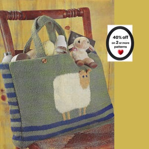 May include: A knitted olive green tote bag featuring a large white sheep motif with a tan face on the front. The bag has dark blue horizontal stripes along the sides and bottom, two sturdy handles, and contains a small plush sheep toy inside.