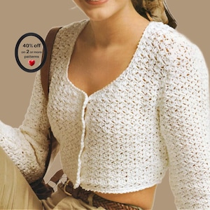 May include: A white long-sleeved cropped cardigan featuring an openwork crochet pattern with a scoop neckline and a front button closure. A circular black badge on the left side displays the text 40% off on 2 or more patterns with a red heart icon.
