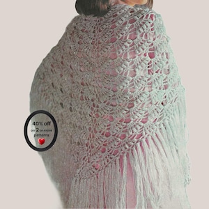 May include: A light mint green triangular crochet shawl featuring an intricate openwork fan pattern and long fringe along the bottom edges. A circular black badge on the left side displays the text 40% off on 2 or more patterns with a red heart.