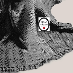 May include: A dark gray knitted blanket featuring a textured chevron pattern and a fringed edge. A white rectangular label is overlaid on the fabric, displaying the text 40% off on 2 or more patterns with a small red heart icon.