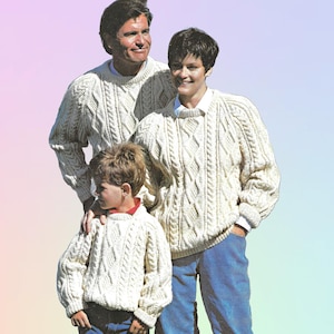 Puede incluir: Tres personas con suéteres de punto trenzado color crema y vaqueros azules. Los suéteres tienen un diseño texturizado y tejido. La familia está de pie junta, con el niño al frente. El fondo tiene un degradado de colores.