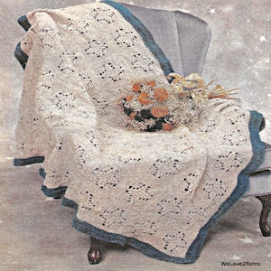 Könnte beinhalten: Eine beige Strickdecke mit quadratischem Muster und einem dunkel-türkisfarbenen Rand. Die Decke liegt über einem Stuhl und ist mit einem Bündel getrockneter orangefarbener und brauner Blumen verziert. Der Text WeLove2Retro ist sichtbar.