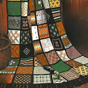 May include: A patchwork quilt with a variety of geometric patterns in shades of green, brown, orange, and white. The quilt is draped over a surface, showcasing its intricate design and textured appearance. The quilt has a black fringe.