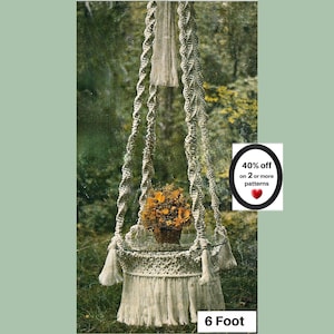May include: A hanging macrame plant stand with a circular glass top, featuring twisted cord supports and a fringed base. A bouquet of yellow flowers sits on the glass. Text on the image reads 40% off on 2 or more patterns and 6 Foot.