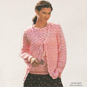 May include: A light pink crochet cardigan and matching shell top set featuring an openwork pattern. The cardigan has long sleeves and a tie-front closure. The shell top has a round neckline. The set is worn over a dark skirt with a floral print.