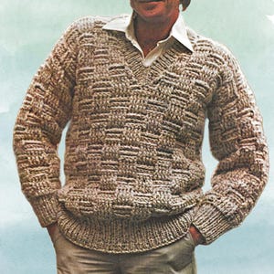 May include: A beige, woven-pattern jumper with a V-neck collar. The jumper has a textured design and ribbed cuffs and hem. A white collared shirt is worn underneath the jumper.