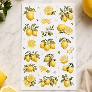 Puede incluir: Una hoja de pegatinas con varias ilustraciones de limones amarillos, incluyendo limones enteros en ramas con hojas verdes y flores blancas, rodajas de limón y gajos, todo dispuesto sobre un fondo rectangular blanco.