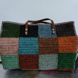 Könnte beinhalten: Eine Patchwork-Tragetasche mit verschiedenen Farben wie Grün, Rosa, Blau, Braun und Orange. Die Tasche hat braune Ledergriffe und einen abnehmbaren Schultergurt. Die Tasche ist aus gewebtem Material.