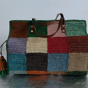Könnte beinhalten: Eine mehrfarbige Patchwork-Tragetasche mit braunen Ledergriffen und einer dekorativen Quaste. Die Tasche besteht aus gewebtem Material und hat Quadrate in Grün, Braun, Rot und Blau.