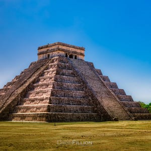 May include: A large, ancient stone pyramid with a flat top and many steps. The pyramid is made of light brown stone and is set against a bright blue sky.