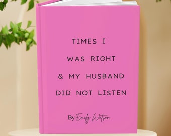 May include: A pink journal with the text "TIMES I WAS RIGHT & MY HUSBAND DID NOT LISTEN" and "By Emily Watson" in black. The journal is open, revealing white pages. The journal is on a white pedestal.
