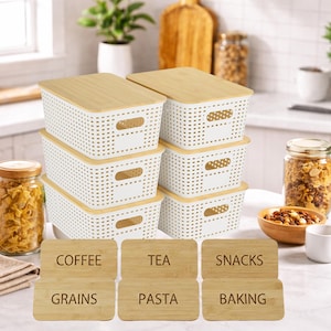 May include: A set of six white plastic storage bins with bamboo lids. Each bin has a rectangular shape with a perforated design and handles. Six wooden labels are included, with text that reads "Coffee", "Tea", "Snacks", "Grains", "Pasta", and "Baking".