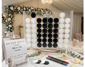 Puede incluir: Un juego de libro de visitas de acrílico transparente con fichas en forma de corazón en blanco y negro. El juego tiene las palabras "Guest Book" en la parte superior. Un letrero junto al juego dice "Guest Book, Help us keep memories".