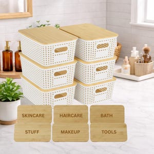 May include: A set of six white plastic storage bins with bamboo lids. Each bin has a rectangular shape with a perforated design. The bins are labeled with wooden tags that read "SKINCARE", "HAIRCARE", "BATH", "STUFF", "MAKEUP", and "TOOLS".