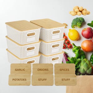 May include: A set of six white woven storage bins with bamboo lids. The bins are rectangular with cut-out handles and are stacked. Six wooden labels are in front of the bins, labeled "Garlic", "Onions", "Spices", "Potatoes", and "Stuff".
