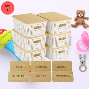 May include: A set of six white storage baskets with bamboo lids. Each basket has a rectangular shape with a woven design and handles. The image includes labels for toys, diapers, books, puzzles, crafts, and memories. A teddy bear and baby toys are also present.